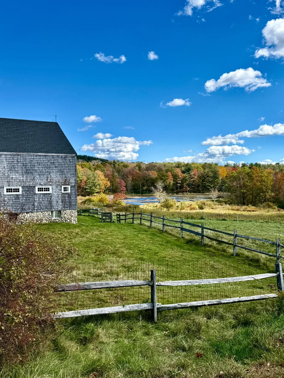 New England autumn landscape with historic barn, rustic wooden fence, and colorful fall foliage under blue sky