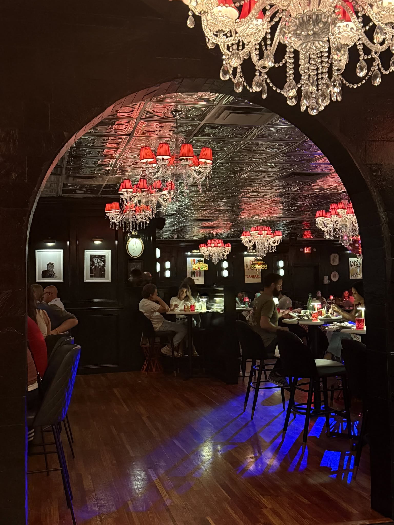 Arthur & Sons dining room viewed through the dramatic arched entrance — chandeliers, pressed tin ceiling, red lamp shades
