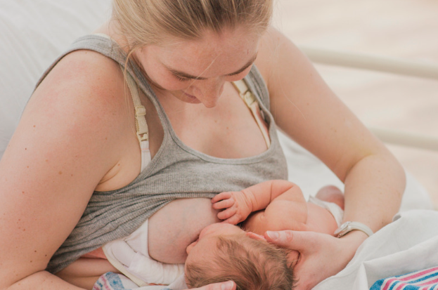 Mother breastfeeding her newborn while supporting the baby's head and body.