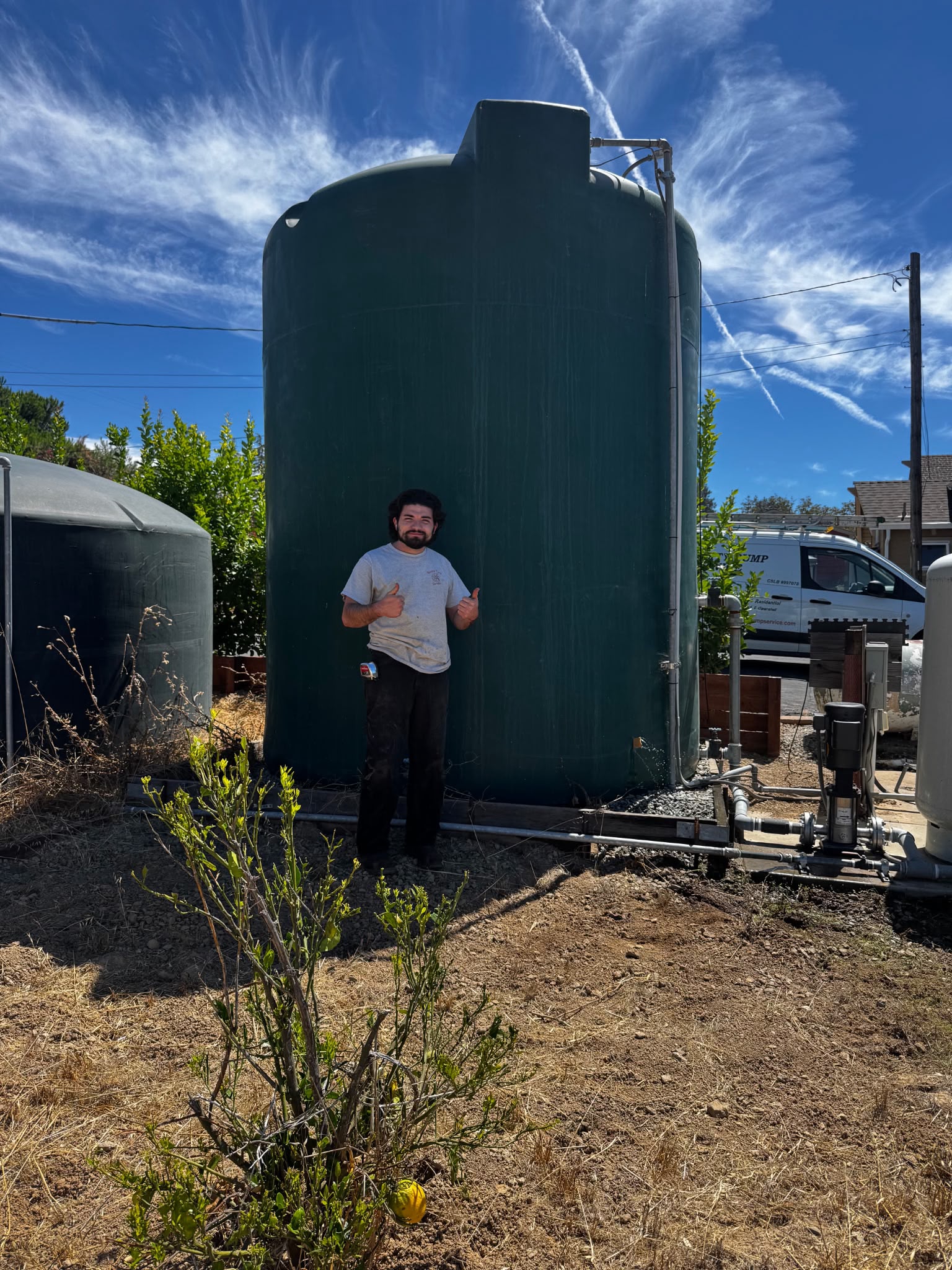 Quality Pump Service technician standing next to a large-capacity commercial water storage tank installation