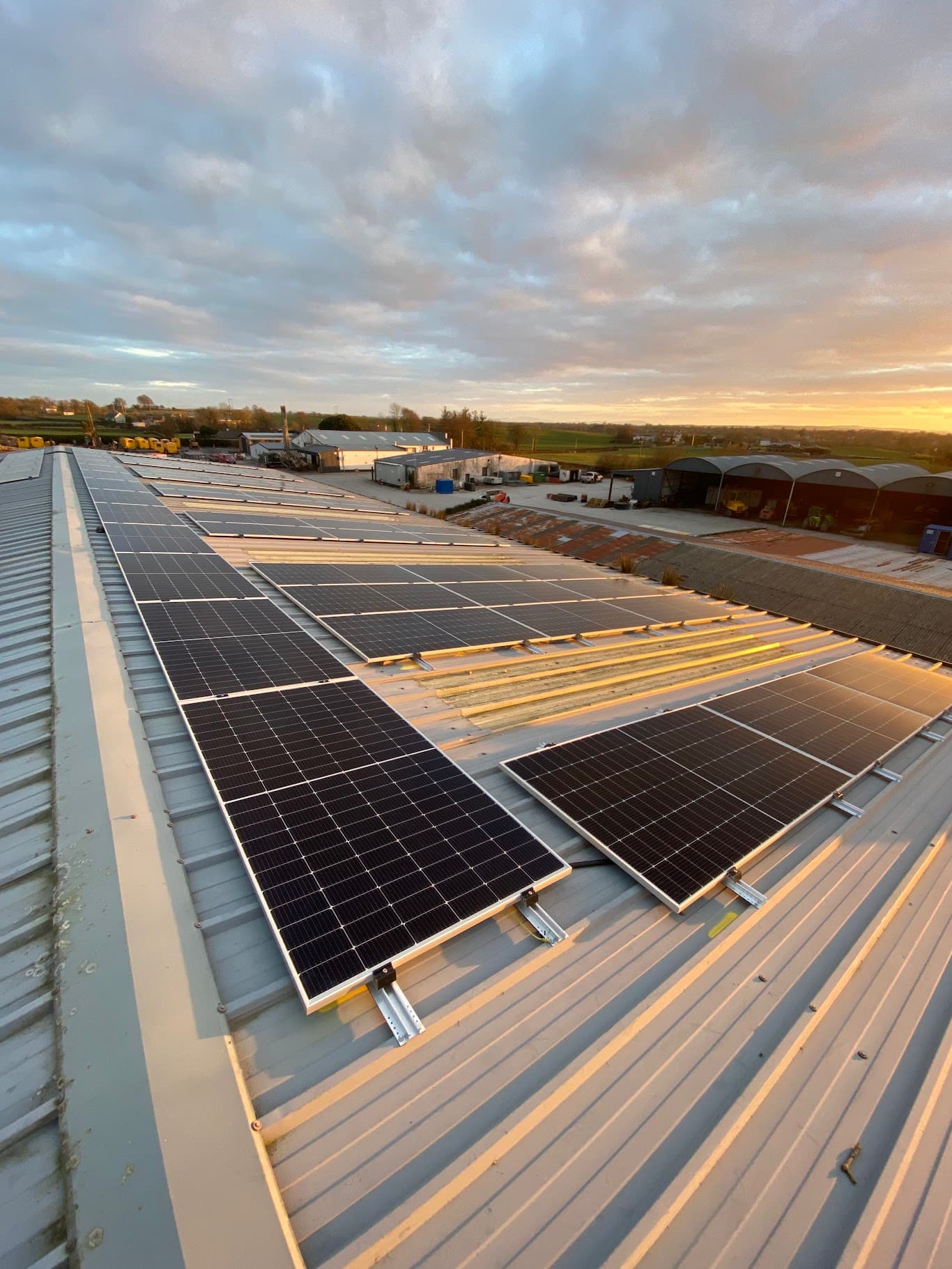 Commercial solar panel array on a large metal roof at sunset