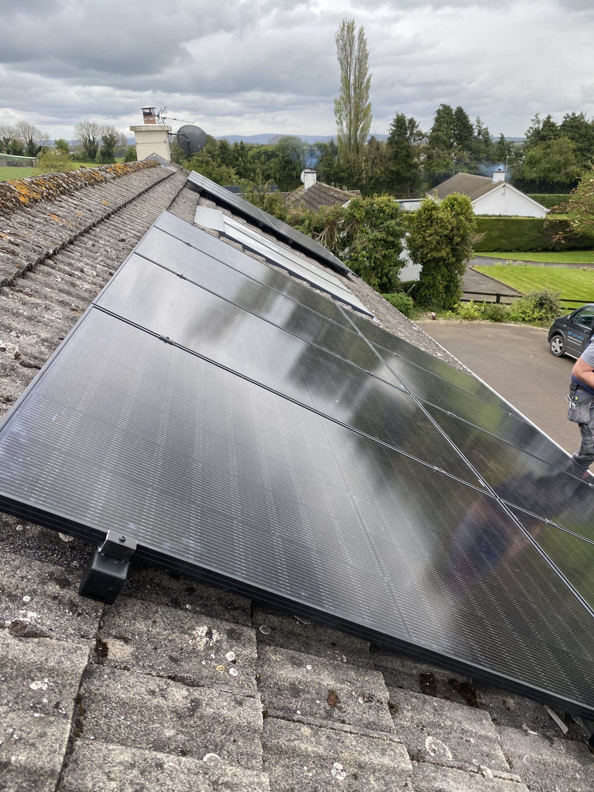 Close-up of all-black solar panels being installed on an Irish roof with Midlands countryside visible