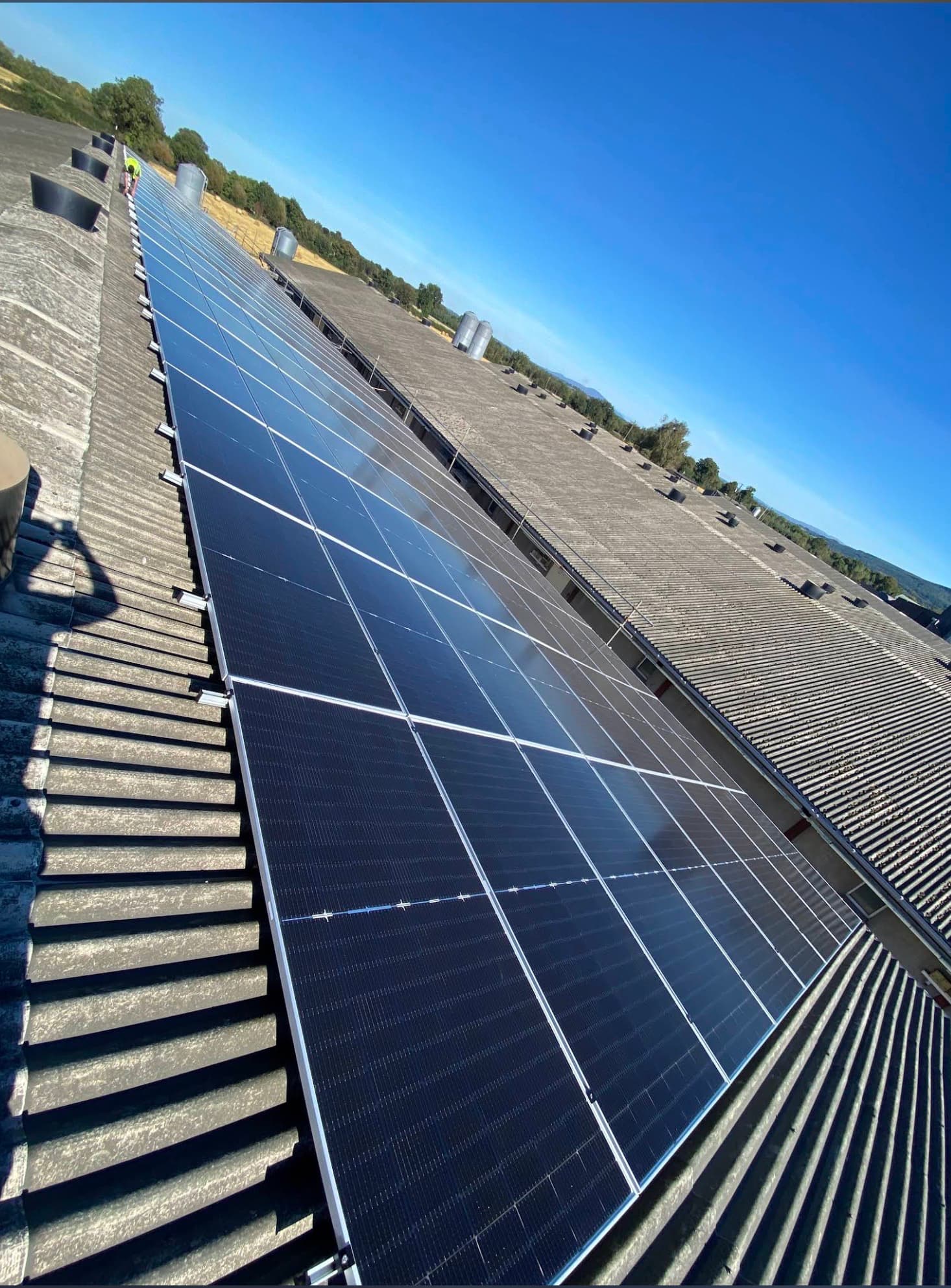 Long-run solar PV array installation across agricultural barn roof under blue sky