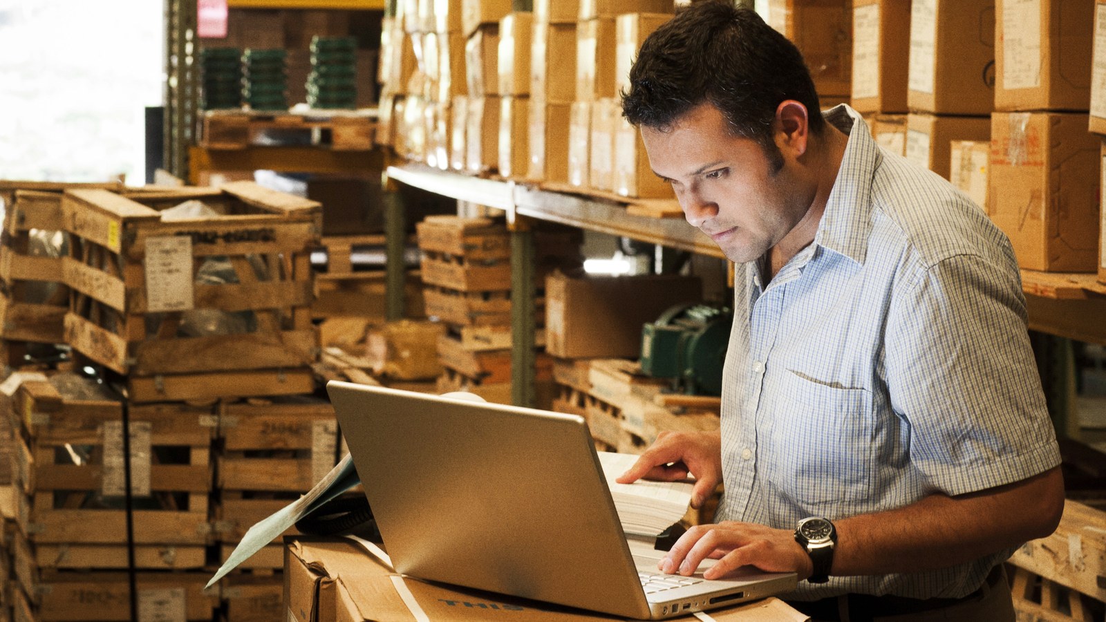 Retail warehouse worker operating laptop near stock boxes.