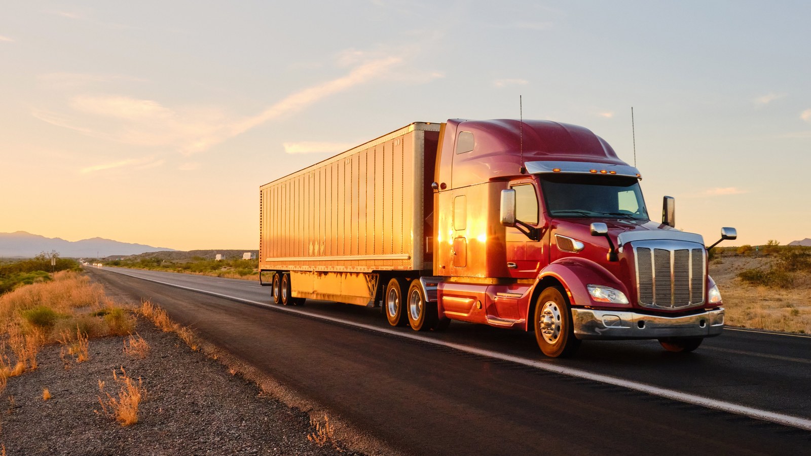 Semi truck hauling a trailer on a highway at sunset.