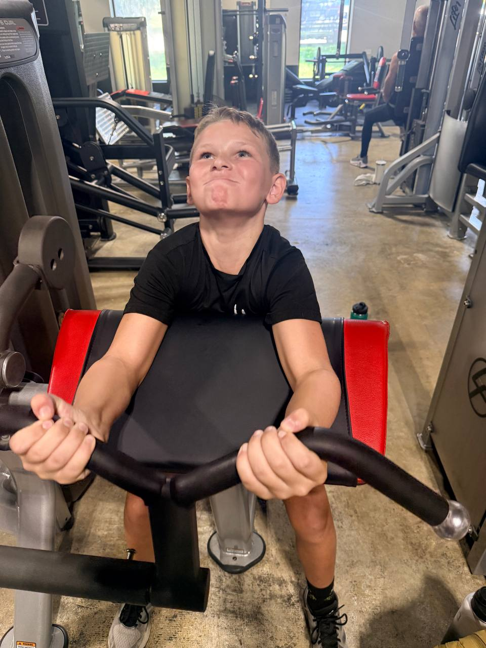 Student athlete performing focused machine bicep curls under athletic training guidance