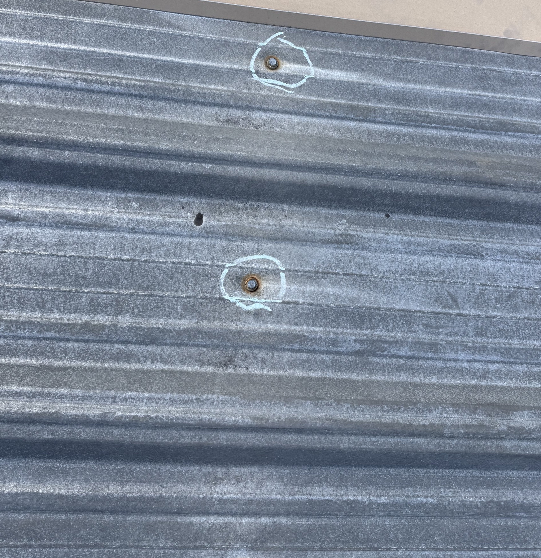 Metal roof panels with two fasteners outlined by light-colored marks