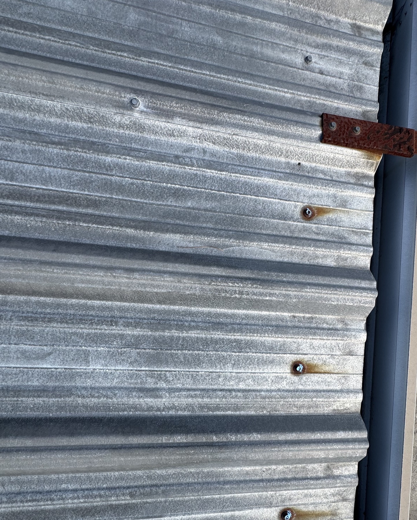 Corrugated metal roof edge with exposed fasteners and a corroded bracket