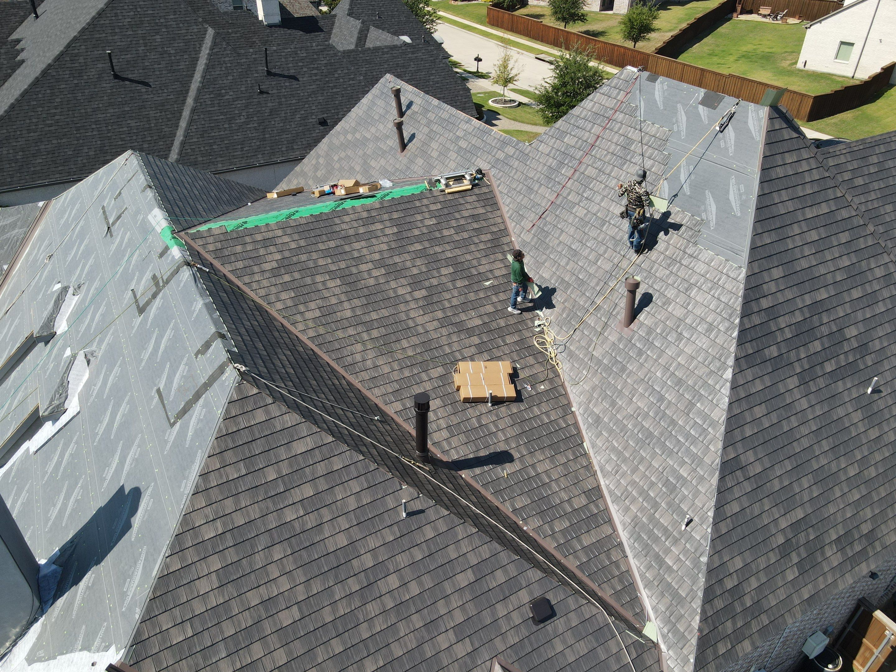 Roofing crew installing metal roof shingles on multi-pitch residential roof