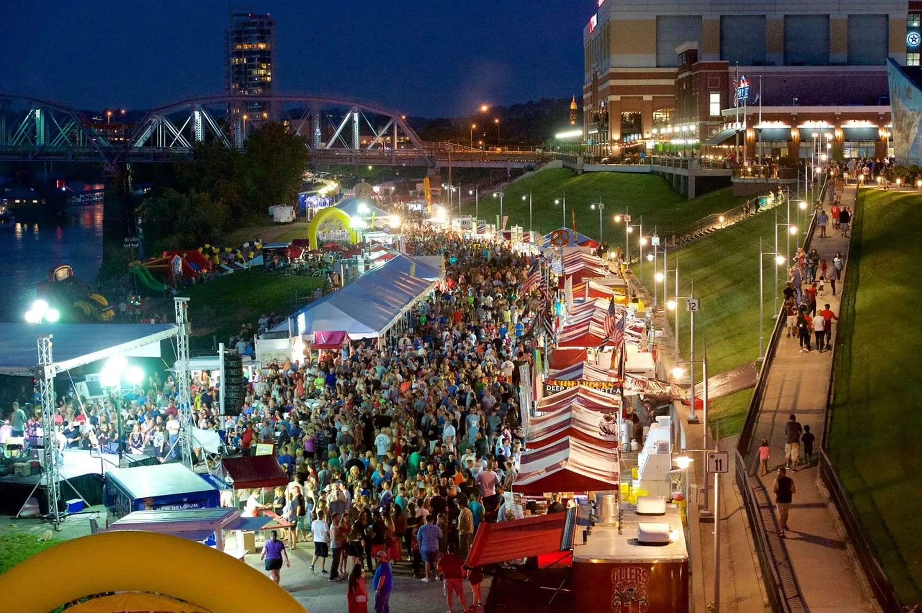 A lively summer food festival along the riverfront in Newport Kentucky, people enjoying sunny weather and eating food, colorful vendor tents