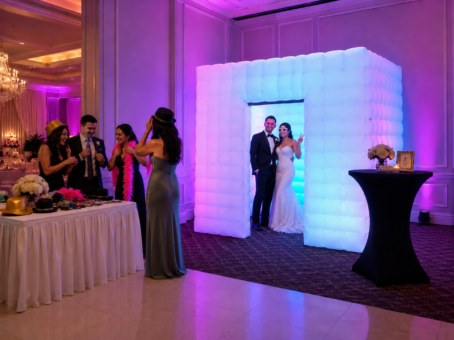Enclosed white square LED inflatable photo booth rental with glowing purple lights and a side door at a Valparaiso Indiana wedding reception, with guests putting on props.