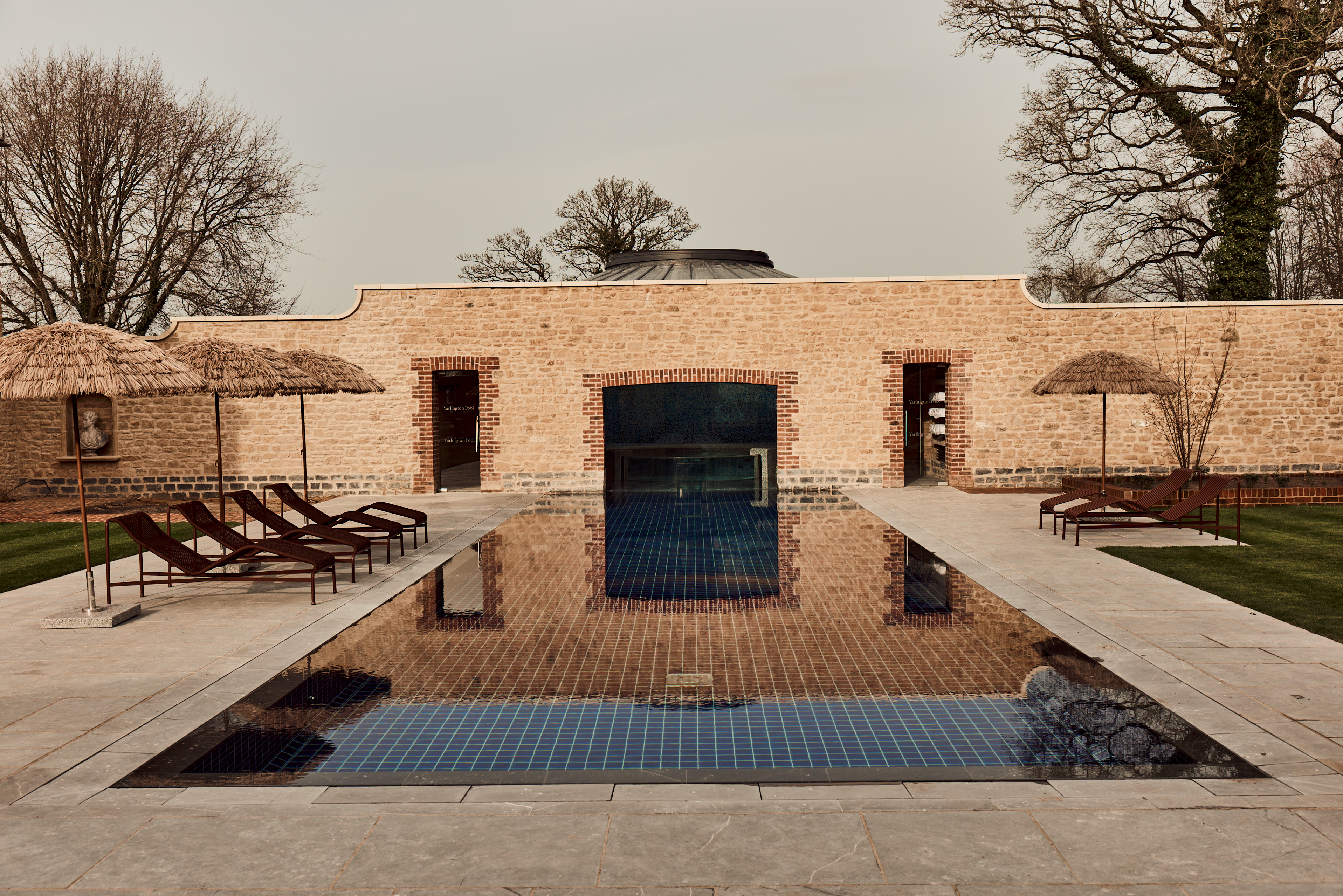 Bespoke courtyard swimming pool with stone pavilion and sun loungers by Poolcourt