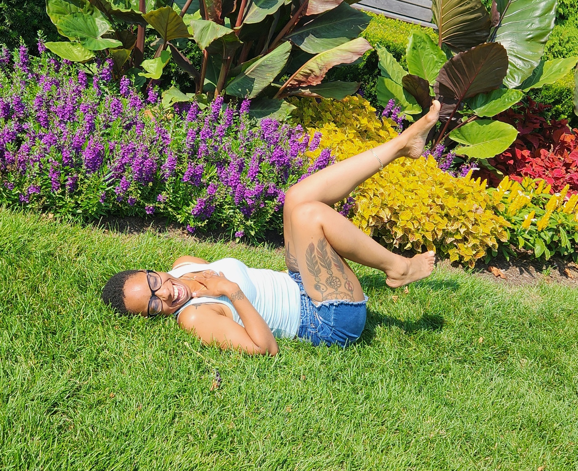 Woman laughing joyfully lying on green grass next to colorful flowers
