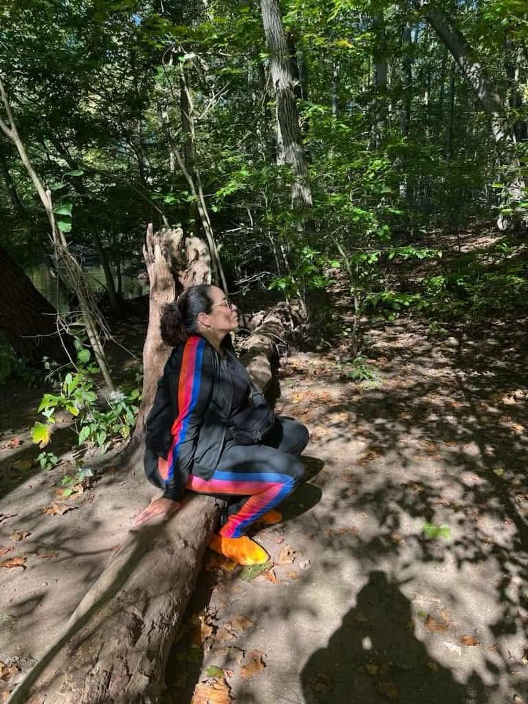 Daisy Olivo sitting peacefully on a fallen tree log along a wooded trail in nature