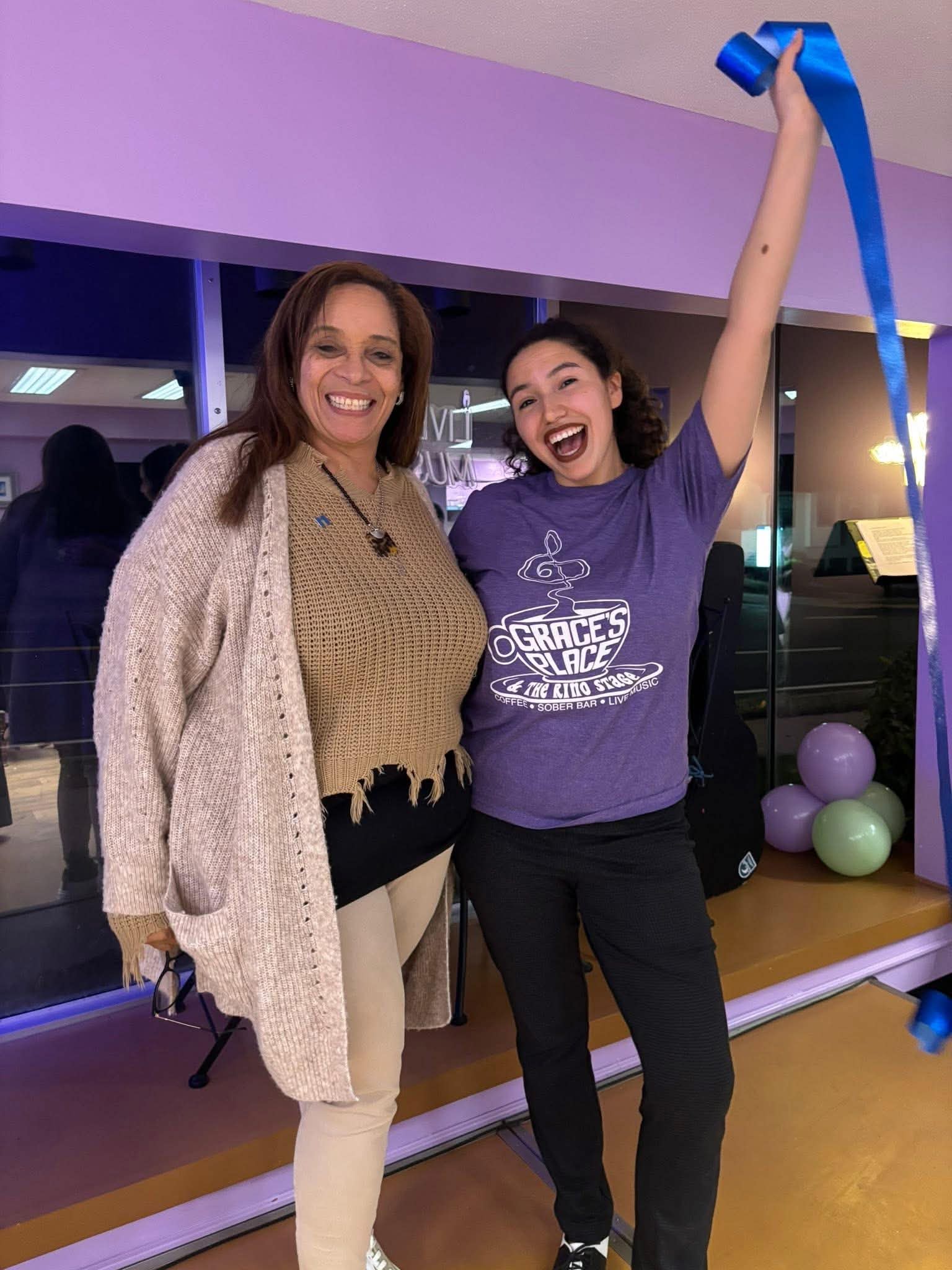 Daisy Olivo celebrating with a fellow advocate holding up a ribbon cutting ribbon at Grace's Place Sober Bar & Live Music