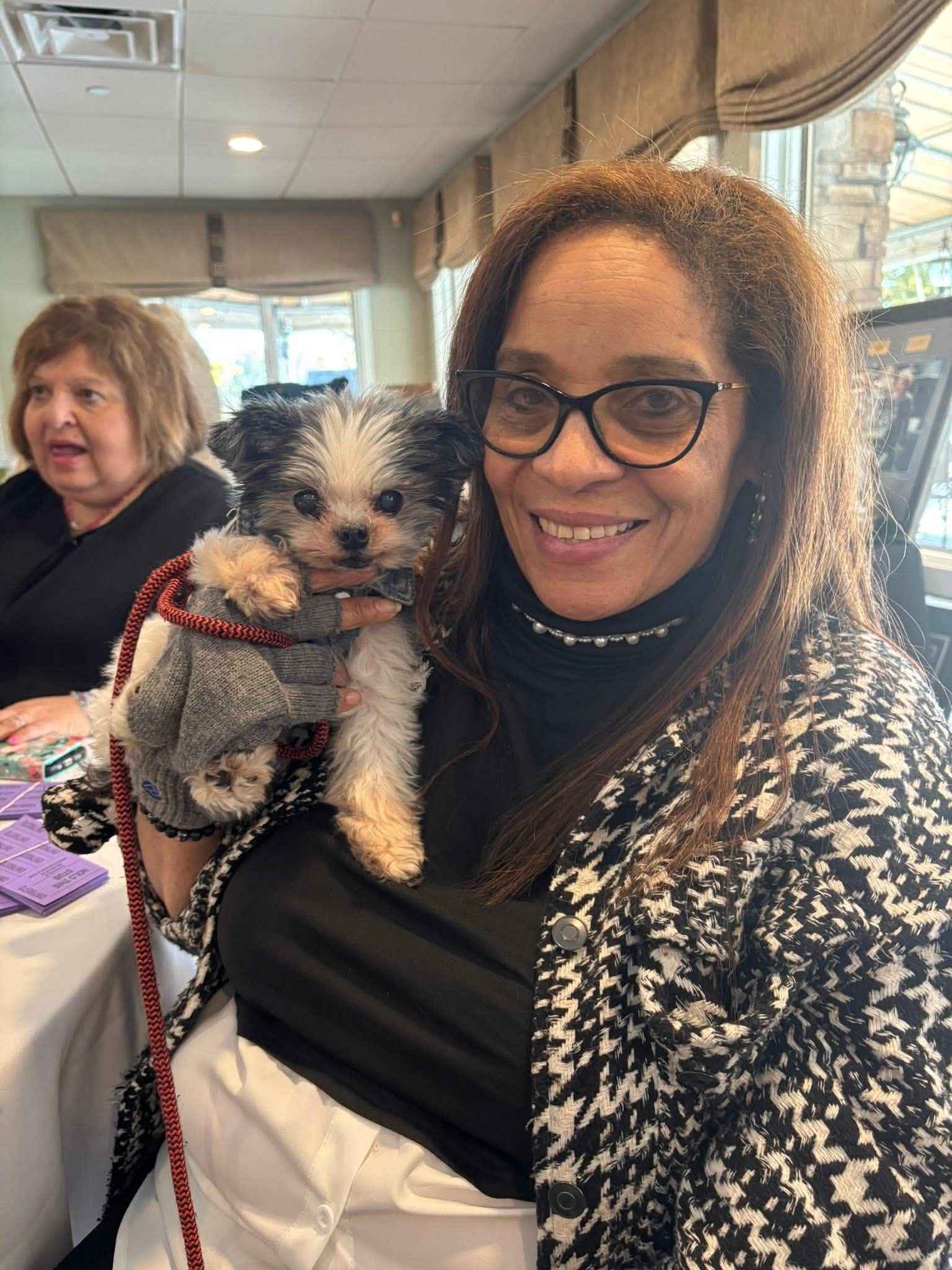 Daisy Olivo warmly holding a small therapy dog dressed in a tiny sweater at a community gathering