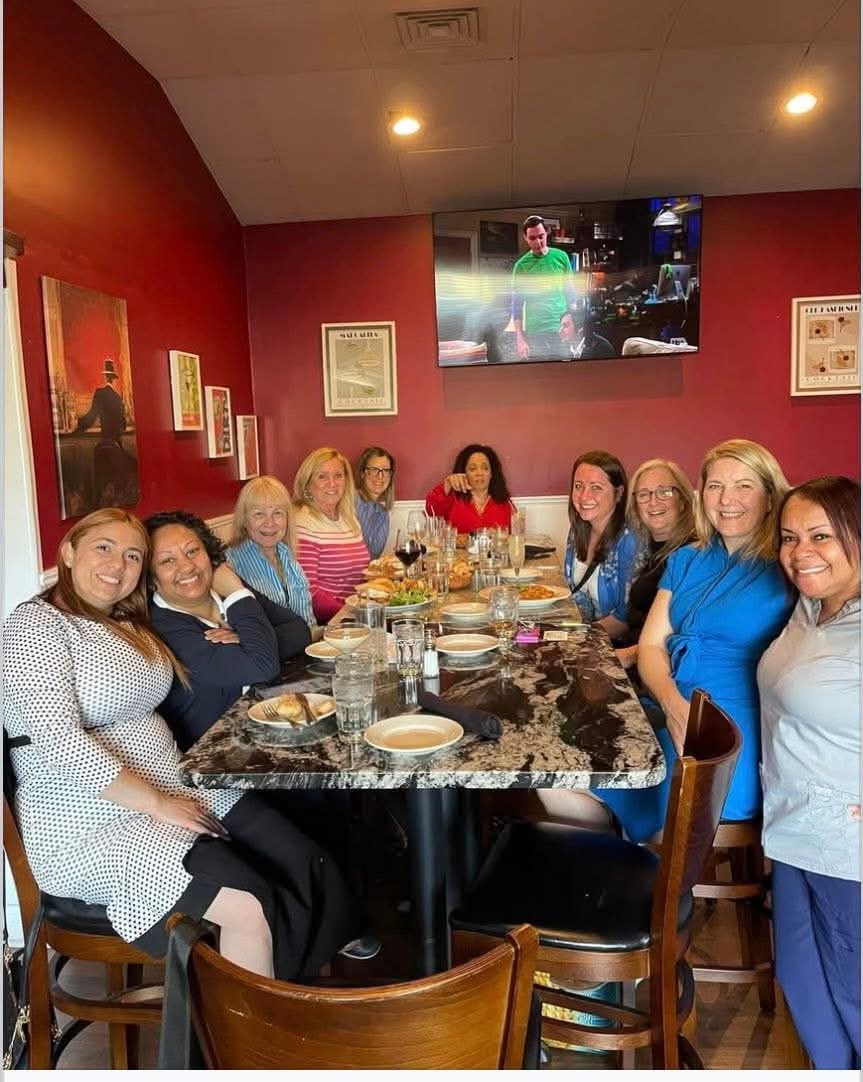 Daisy Olivo seated at a large dining table with a diverse group of women community leaders and healthcare professionals