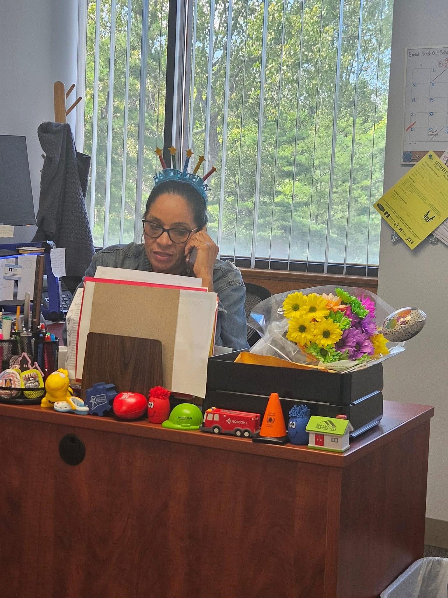 Daisy Olivo at her community office desk taking a phone call surrounded by resources, desk items, and celebration flowers