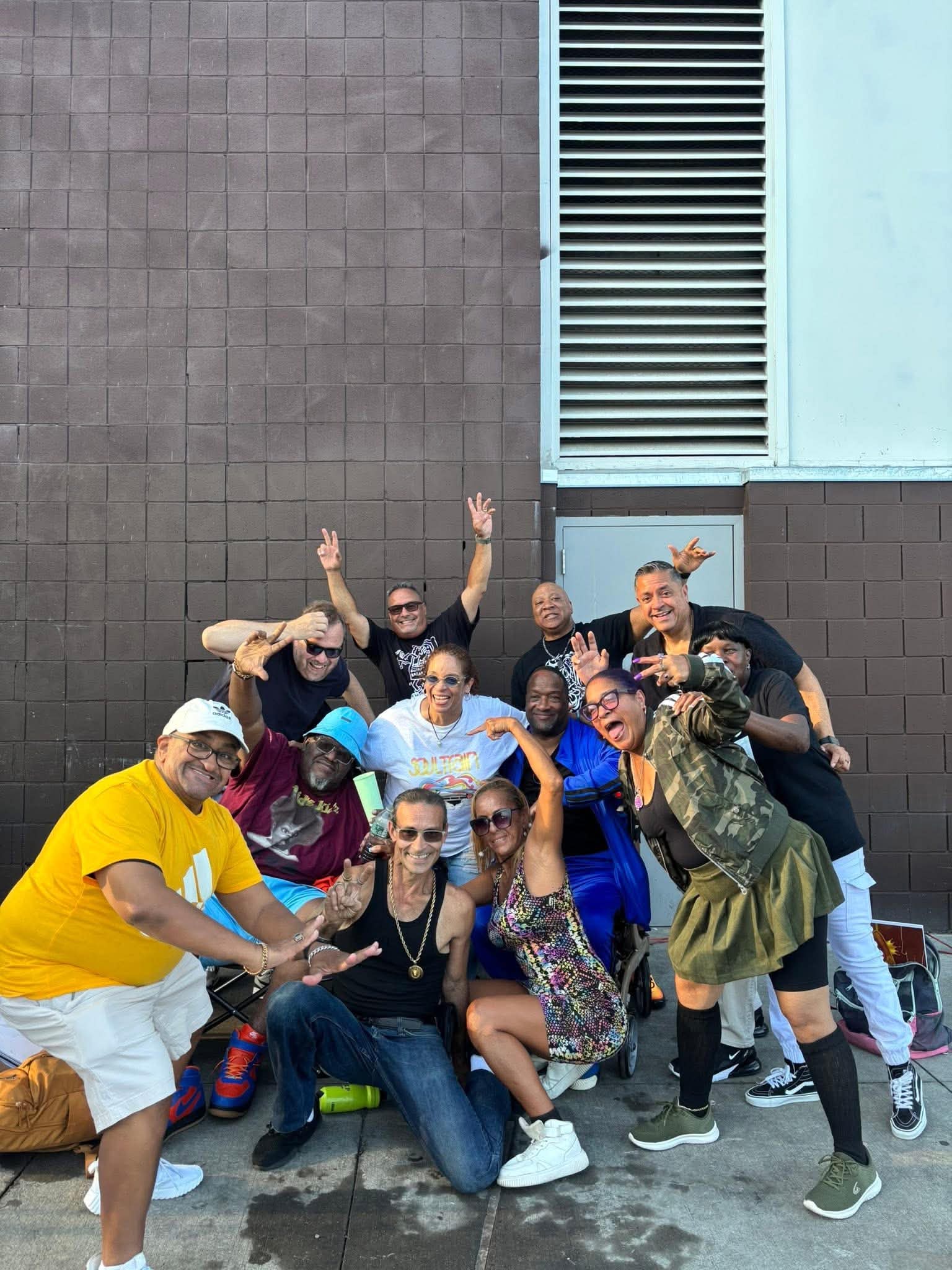 Daisy Olivo celebrating enthusiastically with a large group of diverse community advocates making peace and joy gestures outdoors