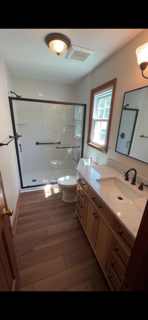 Completed bathroom remodel by Southern Shower Pros - vanity, wood flooring, and frameless glass shower