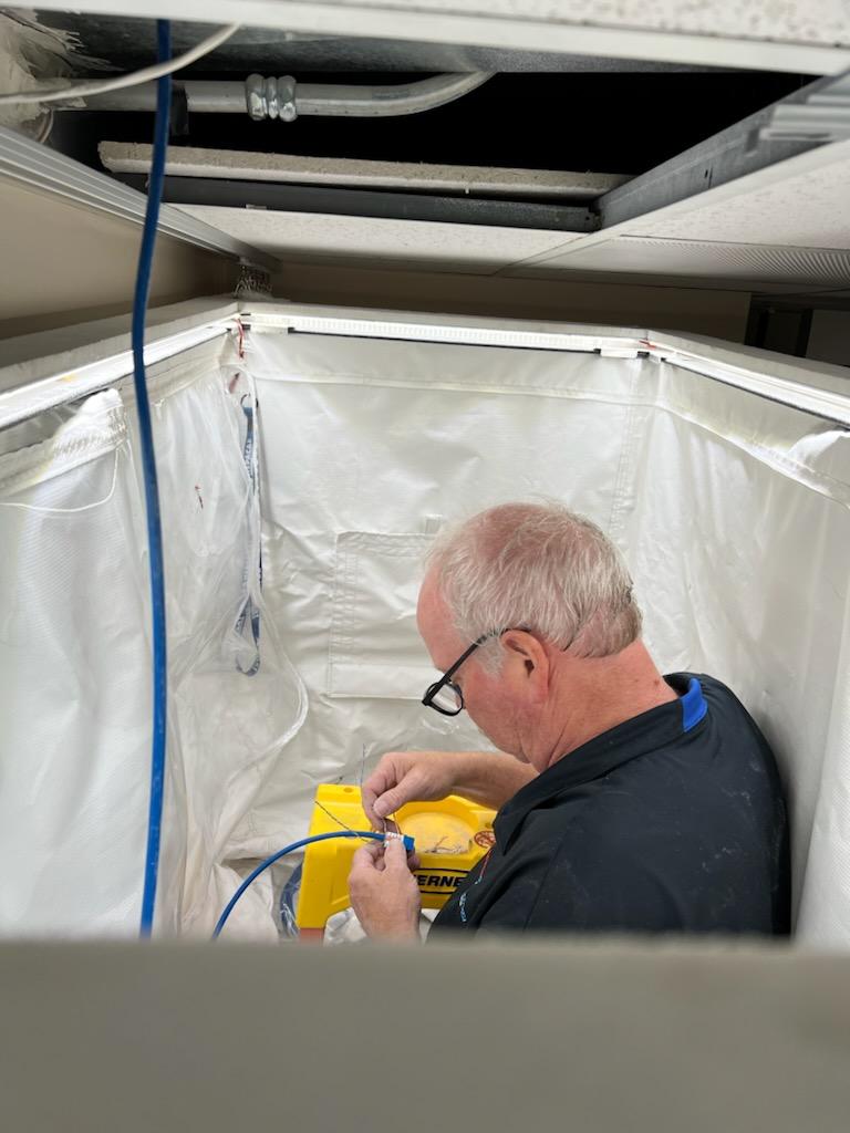 Action Technology Services technician performing sustainment work inside a ceiling containment enclosure