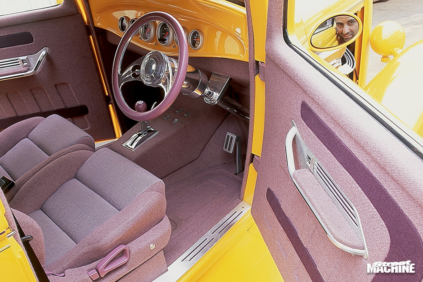 Custom interior of a yellow classic car with purple upholstery and billet steering wheel
