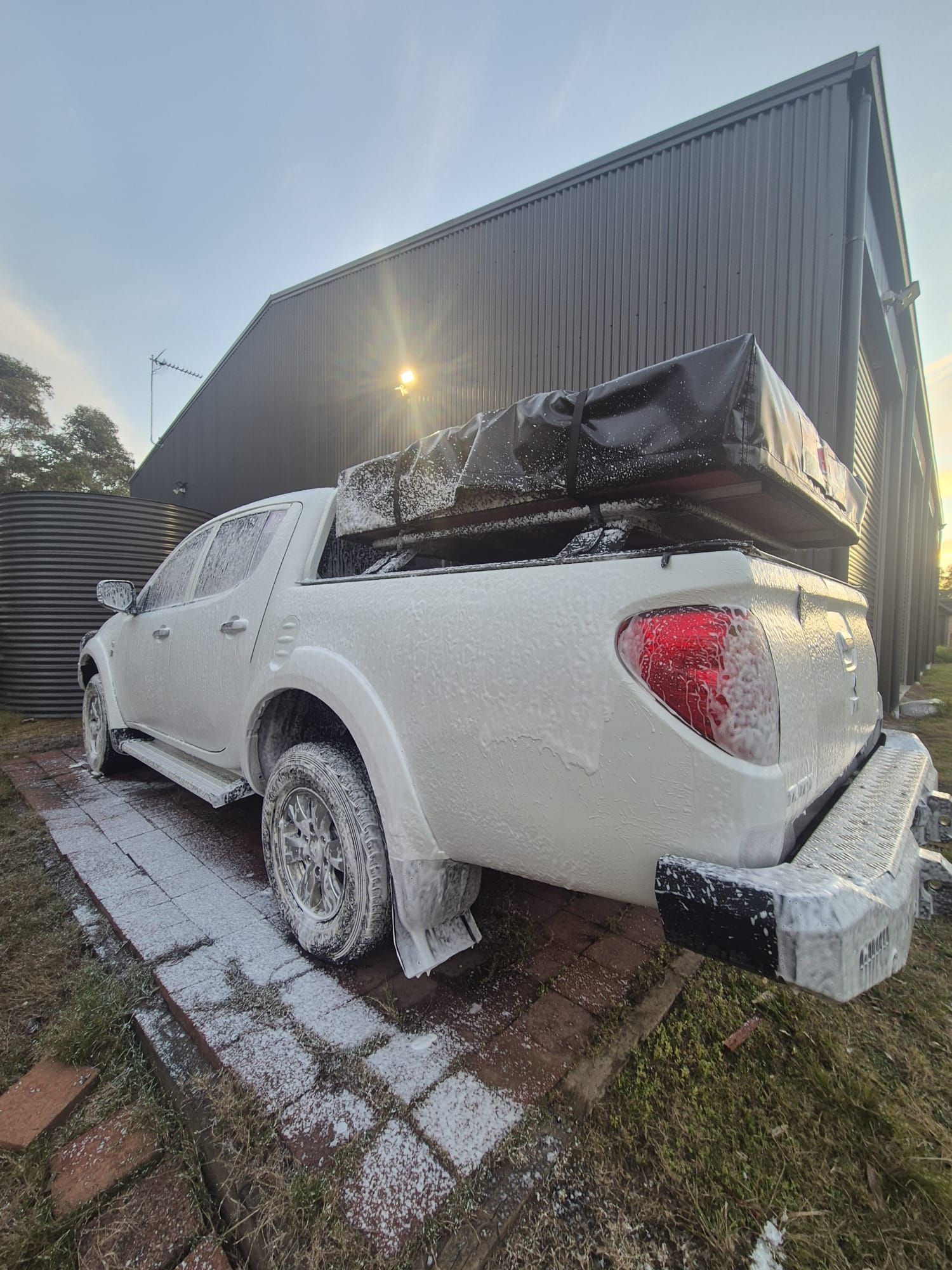 Rear view of Mitsubishi Triton pickup truck covered in thick snow foam during a detailing session at Groom Garage