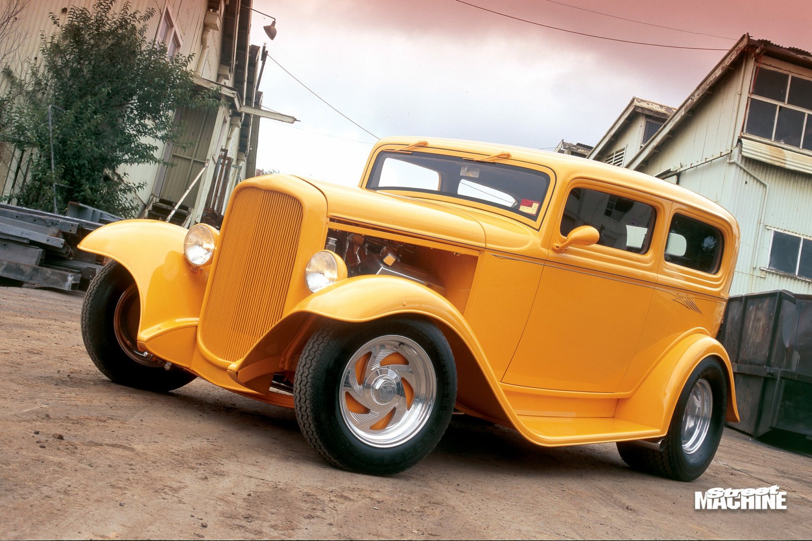 Front angle of a classic yellow Ford hot rod parked outdoors