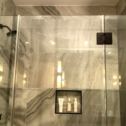 Modern stone shower enclosure with glass door and built-in niche