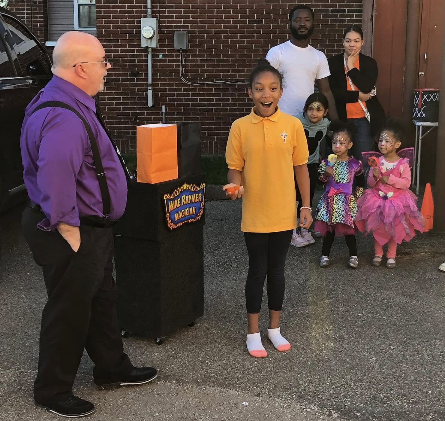 Mike Raymer performing a magic trick for an excited girl and Halloween trick-or-treaters