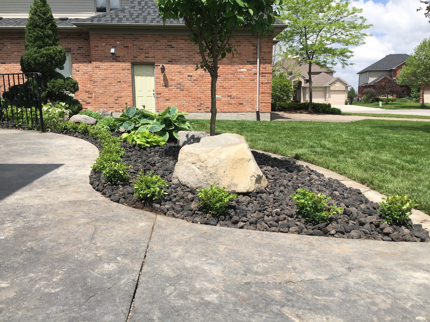 Curved landscape garden bed with decorative boulder and dark rock mulch in London, Ontario