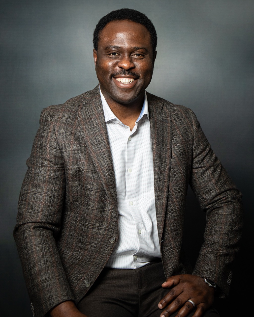 Professional studio headshot — male professional in brown jacket
