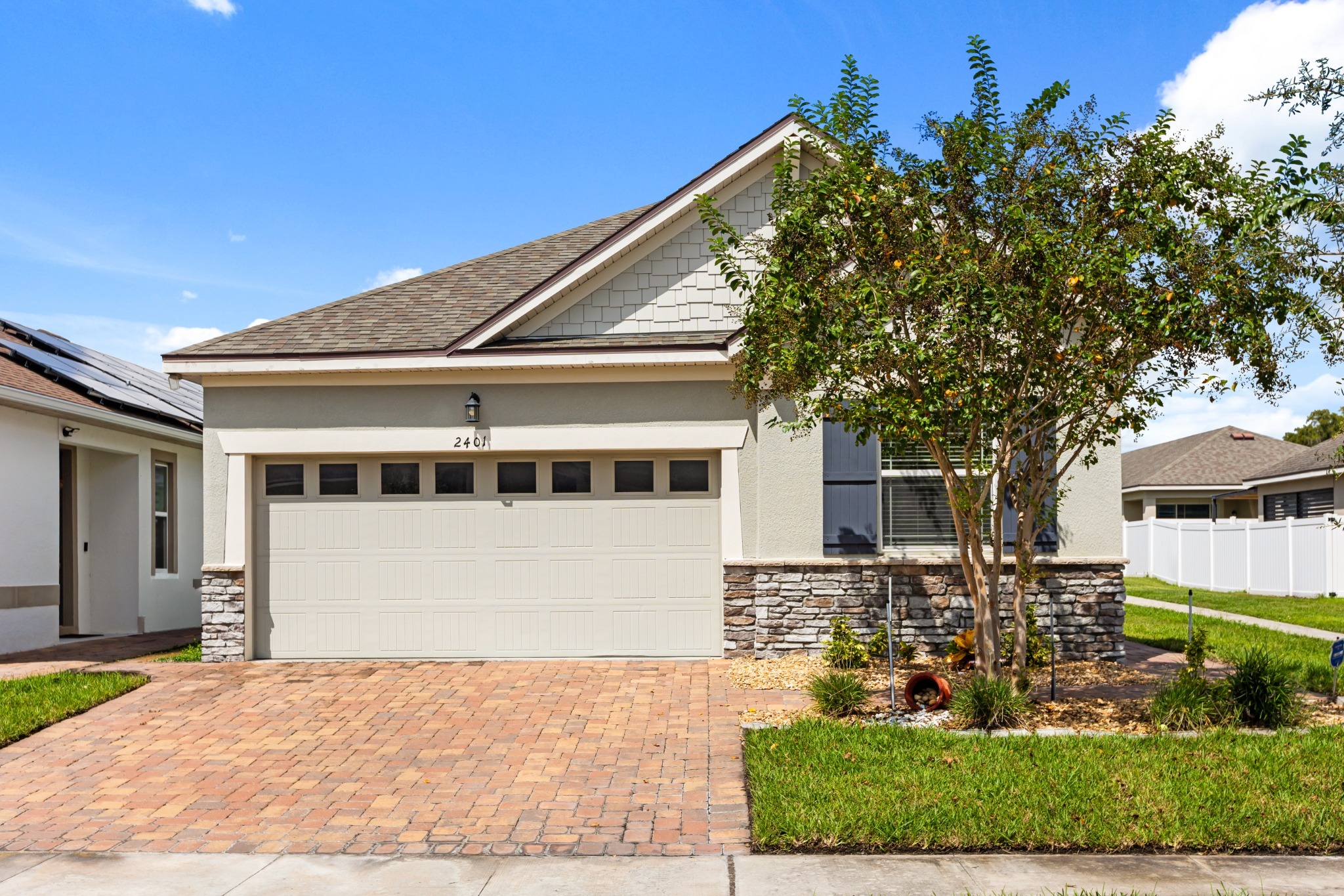 2401 Avian Loop Kissimmee FL - Straight-on front exterior view showing two-car garage, stone wainscoting, decorative coach light, and paver driveway