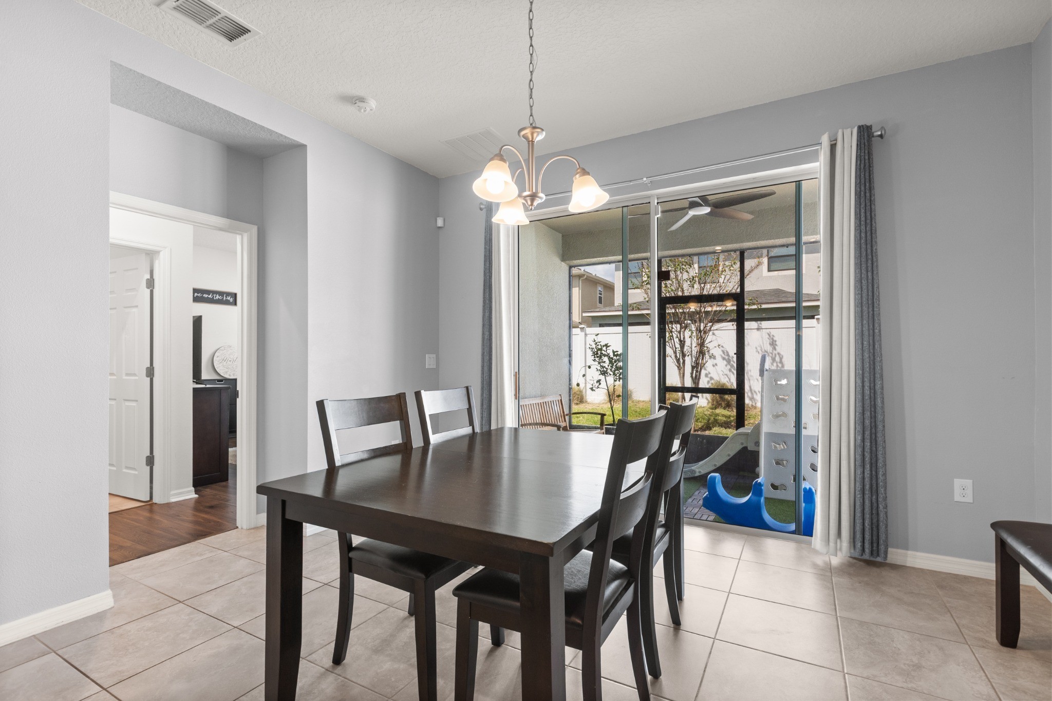 2401 Avian Loop Kissimmee FL - Dining room area with modern chandelier, ceramic tile flooring, and sliding glass doors opening to screened lanai