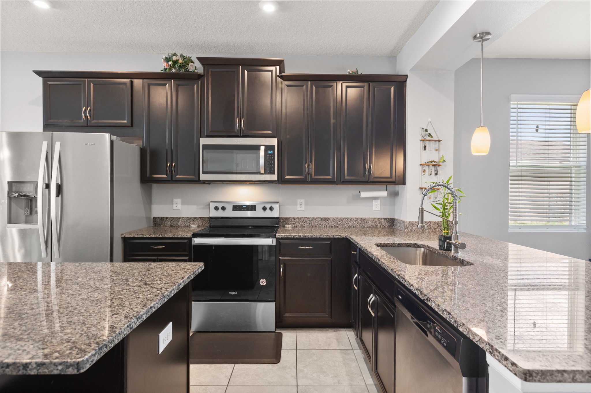 2401 Avian Loop Kissimmee FL - Primary kitchen detail showing granite countertops, dark espresso cabinetry, stainless steel appliances, undermount sink, and counter seating