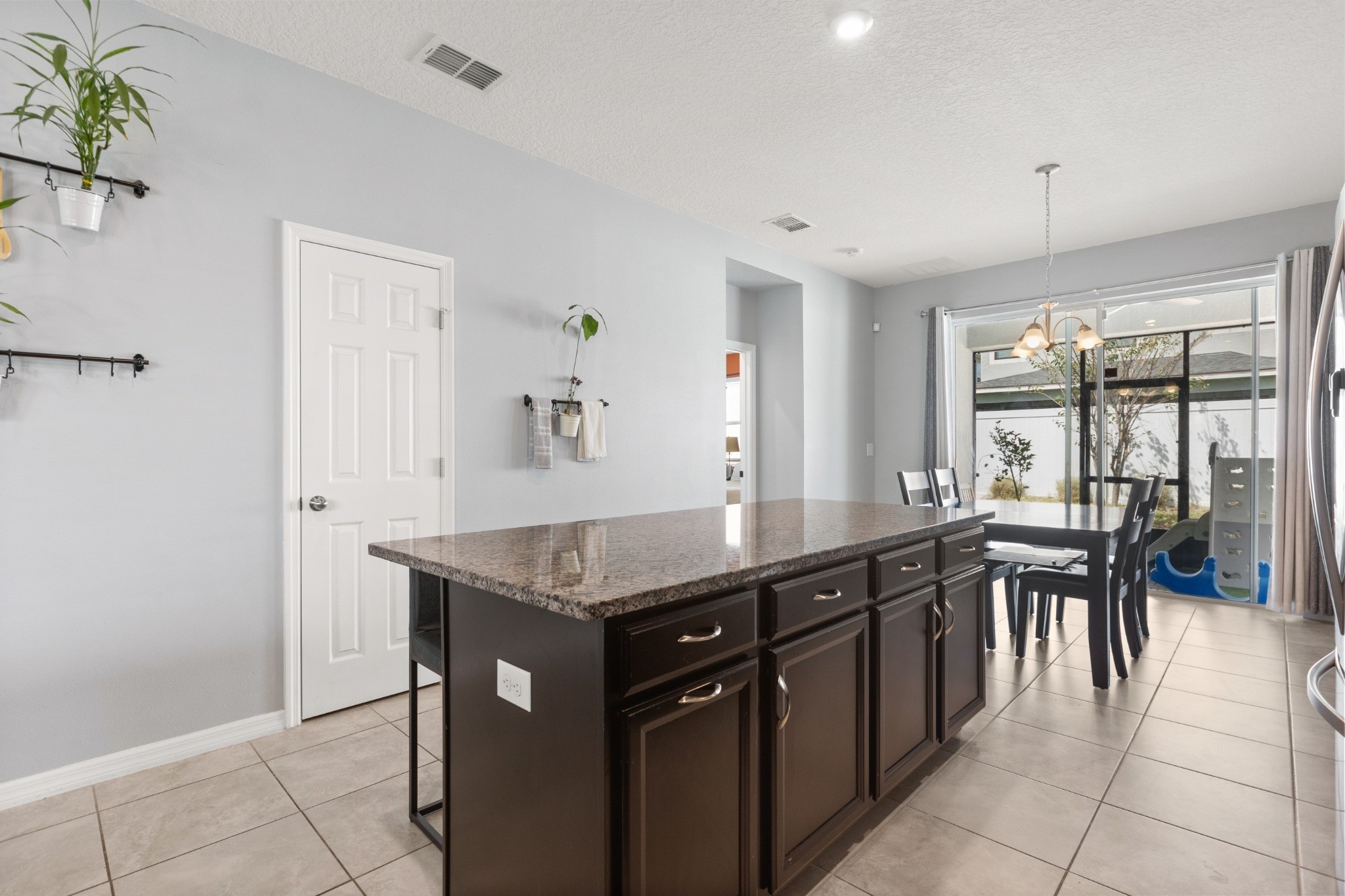 2401 Avian Loop Kissimmee FL - Kitchen island showing granite countertop, cabinetry storage, adjacent dining space, and view toward screened lanai doors