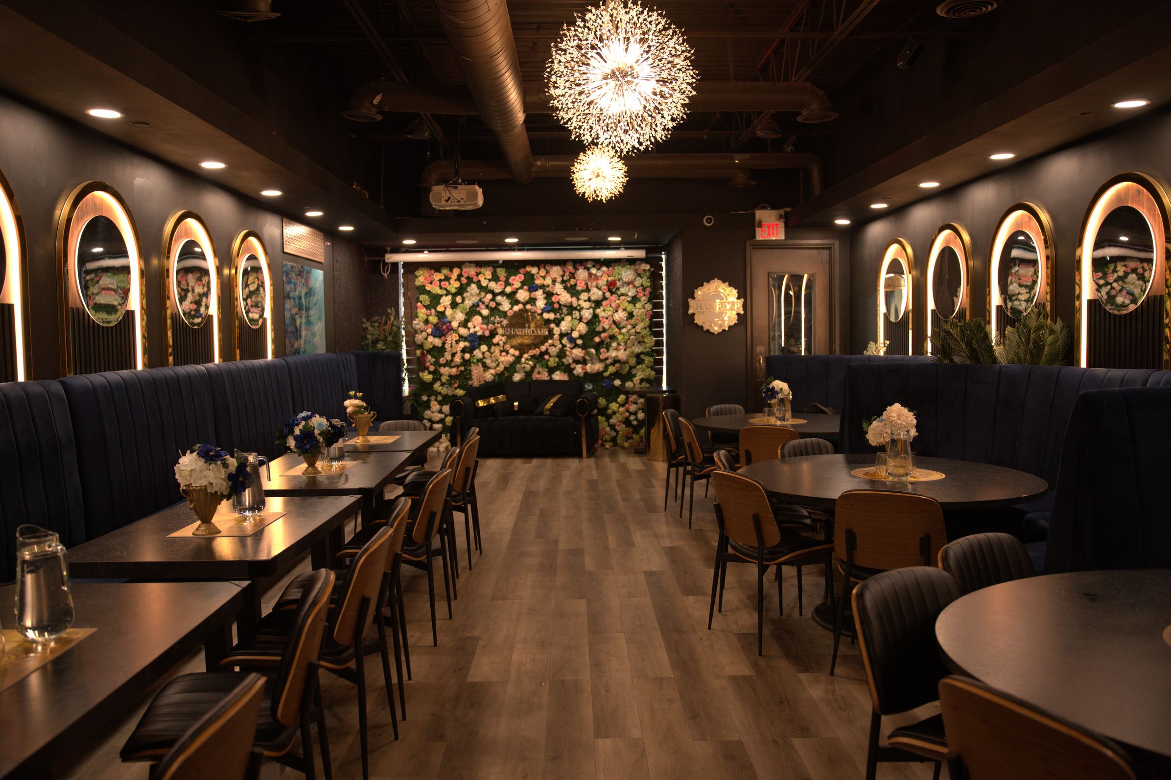 Khatirdari party hall Brampton full view with navy velvet booths, gold arch mirrors, and floral wall backdrop