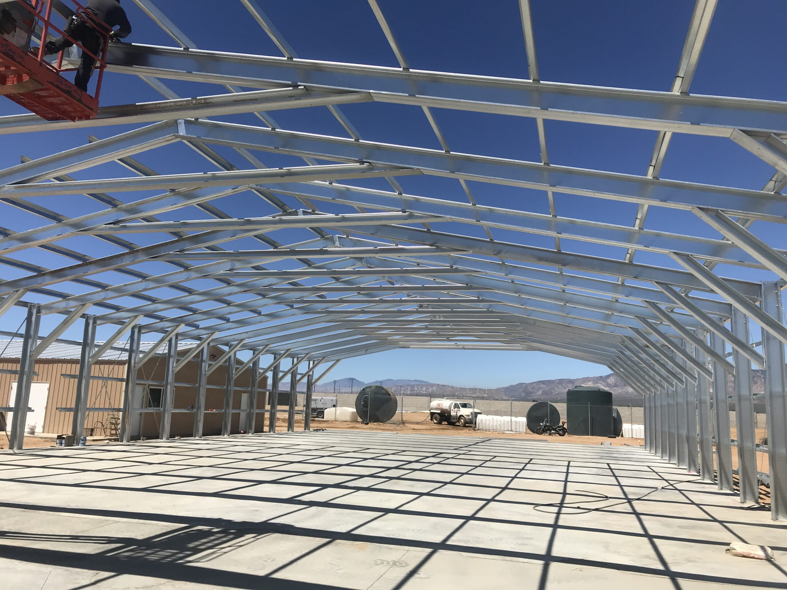 Interior view beneath a long-span galvanized steel roof frame before panels are installed.