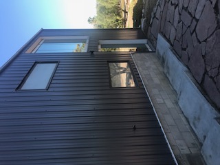 Side view of the dark metal home with stacked windows and a stone path.