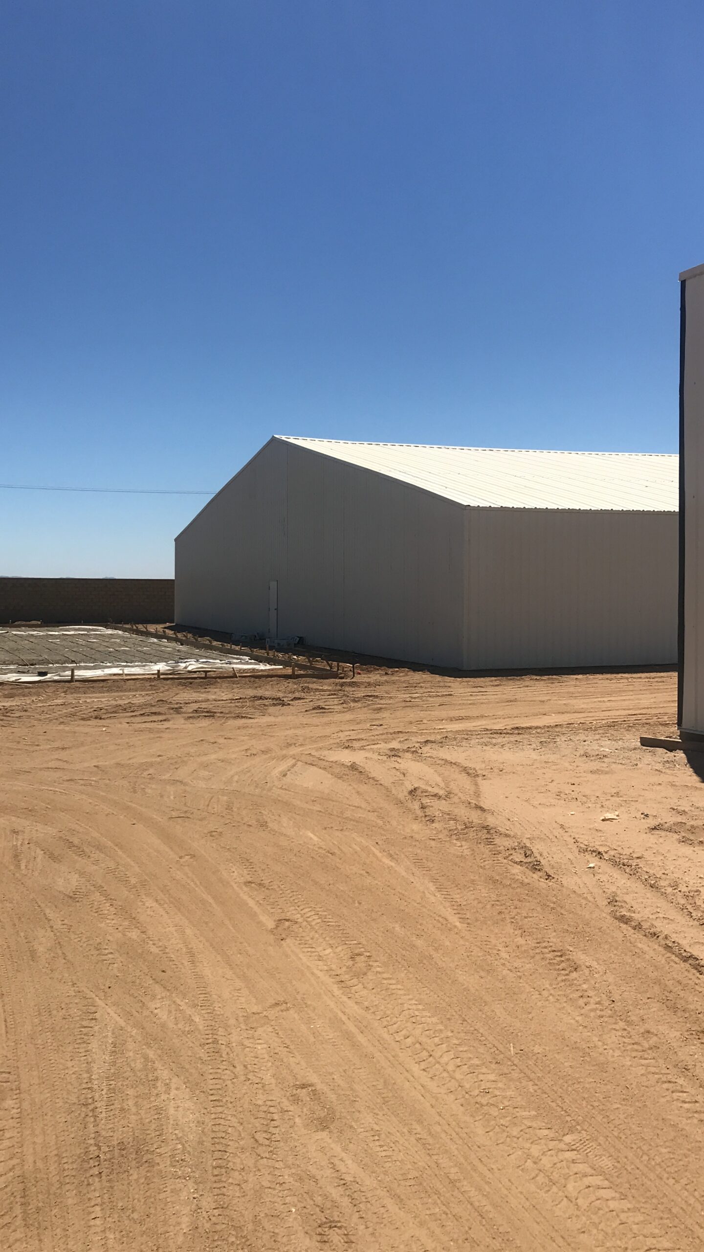 Completed light-colored steel warehouse on an open dirt site.