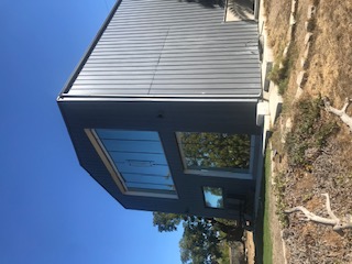 Completed modern two-story home with dark vertical metal cladding and large windows.