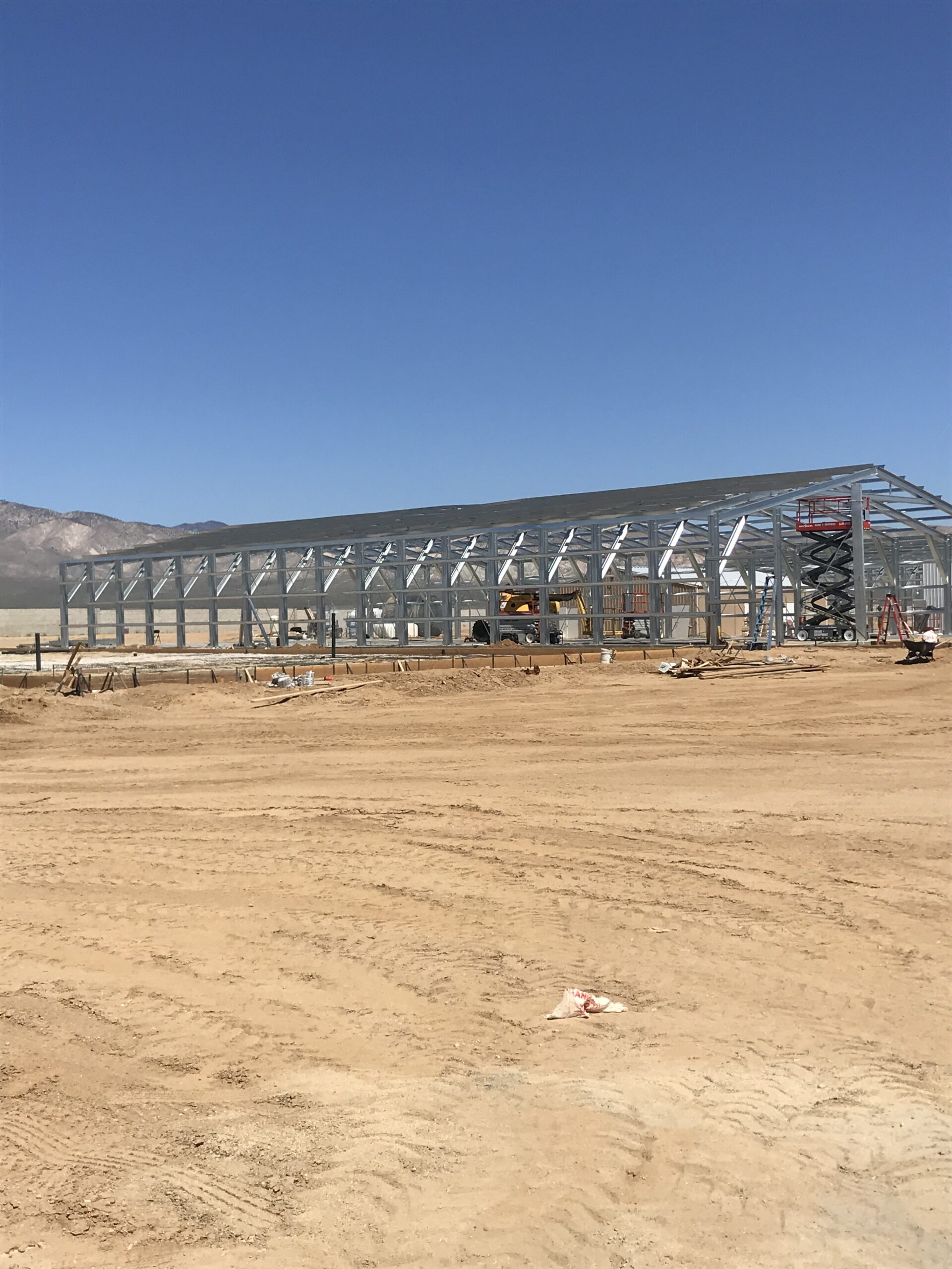 Long galvanized steel building frame erected on a large open construction site.
