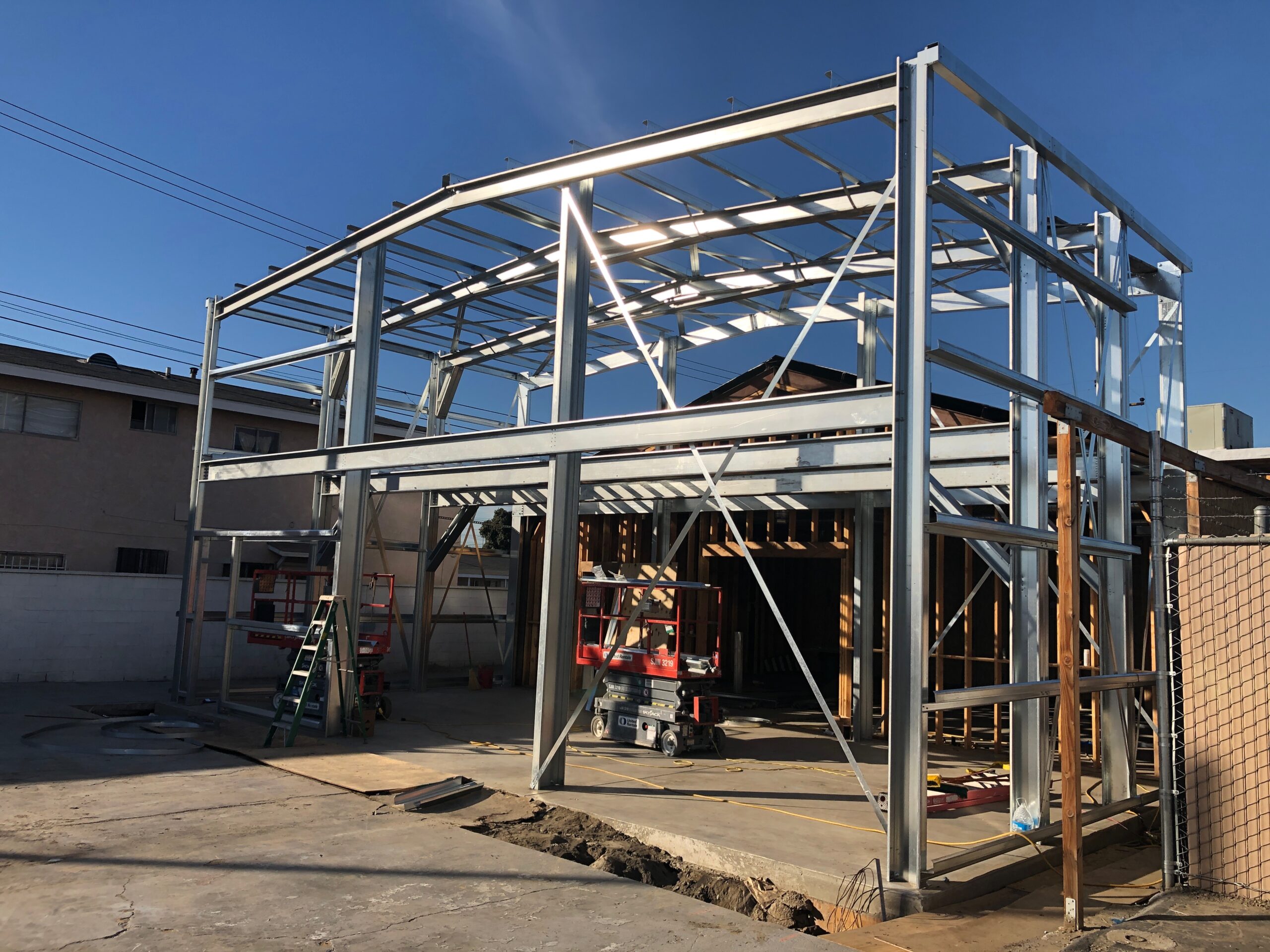 Multi-story galvanized steel building frame erected around an existing wood-framed structure.
