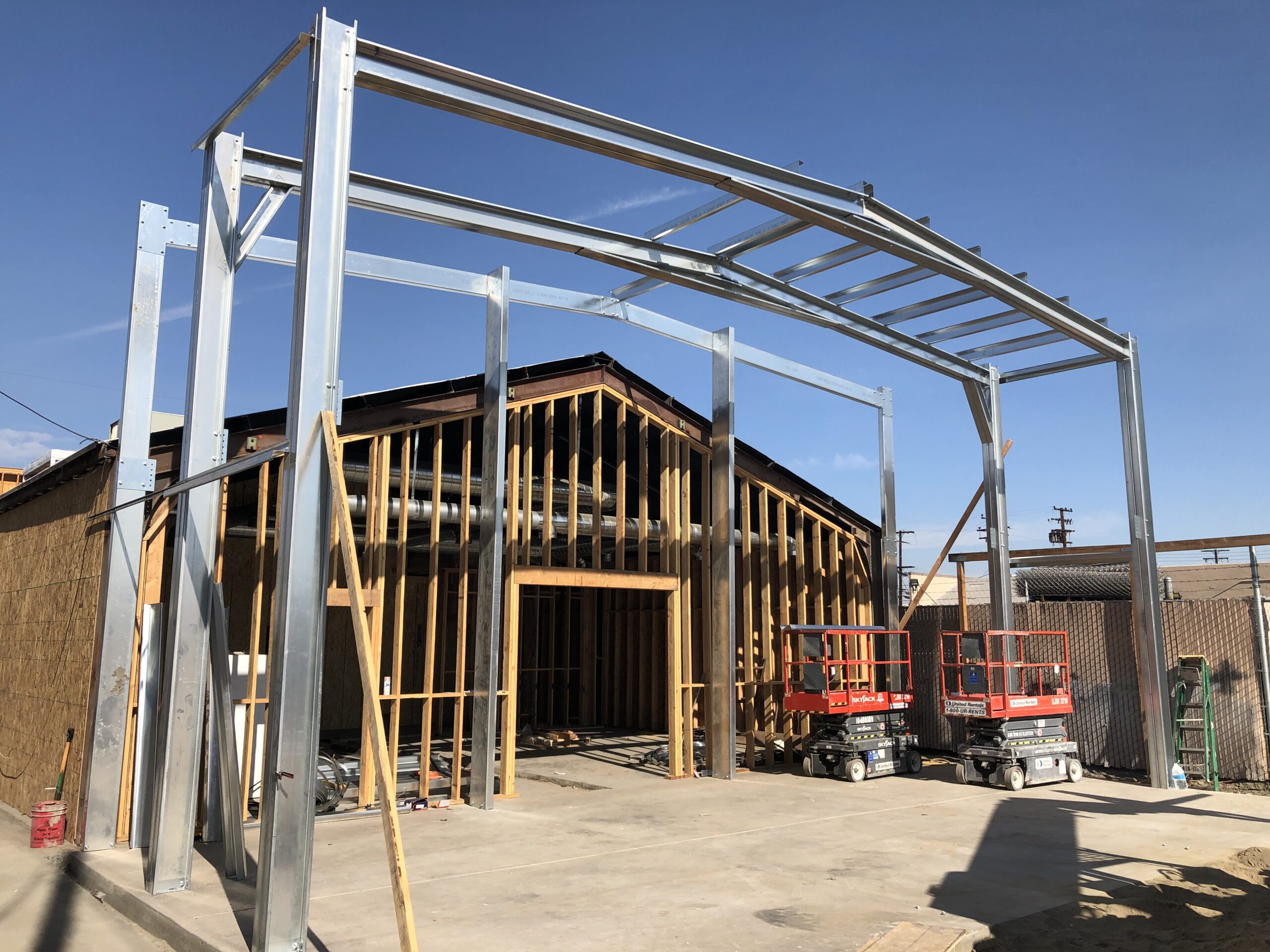 Galvanized steel frame addition under construction beside a wood-framed building.