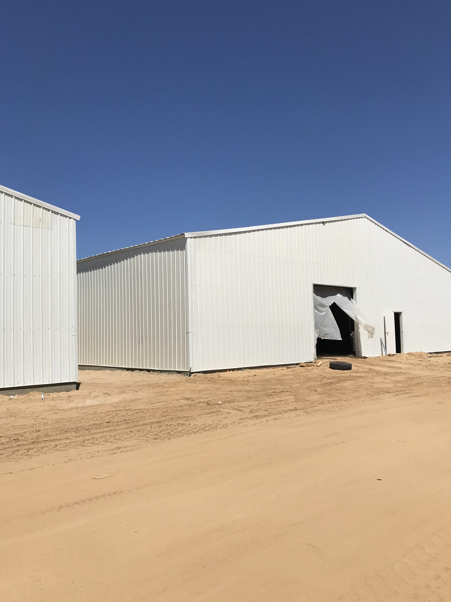 Two completed white steel storage buildings on a graded dirt lot.