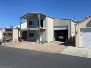 Front view of a finished two-story beige metal shop with an open garage bay.