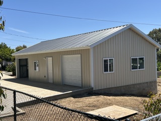 Front and side view of a completed beige metal workshop with a roll-up garage door.