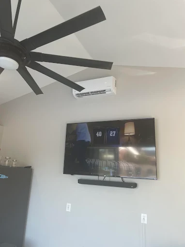 Wall-mounted indoor mini split unit above TV with vaulted ceiling and fan in Boerne home