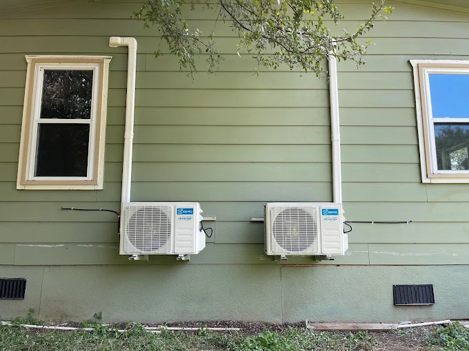 Wall-mounted outdoor dual mini split condensers on green siding exterior in Pearland