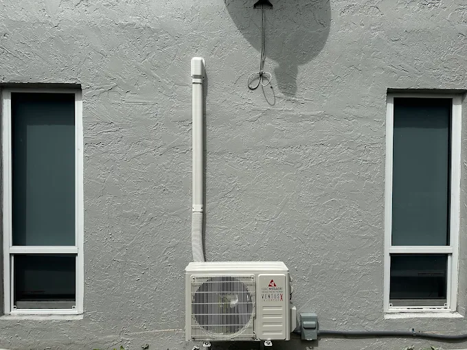 Wall-mounted ductless condenser between windows on home exterior in Schertz